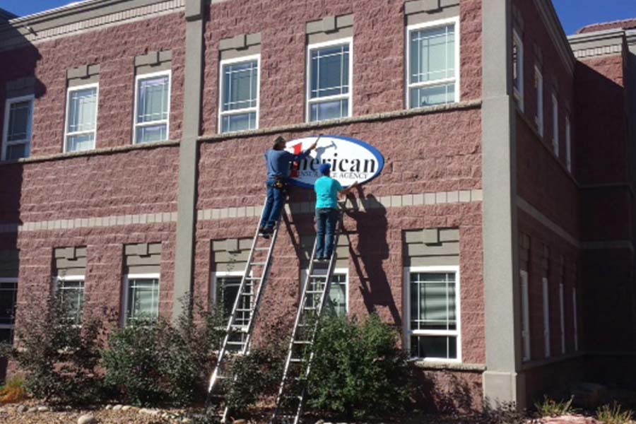 Contact - 1st American Insurance Agency Sign Being Hung on Building with Men on Ladders